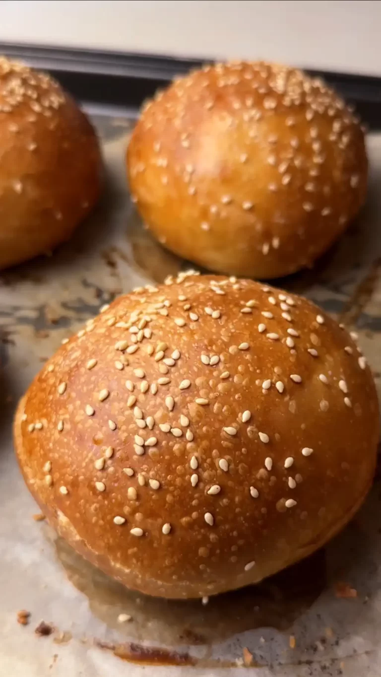 Golden sourdough hamburger buns topped with sesame seeds on baking paper