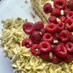 top view of pistachio olive oil cake with thyme buttercream swirls and a pile of raspberries in the middle