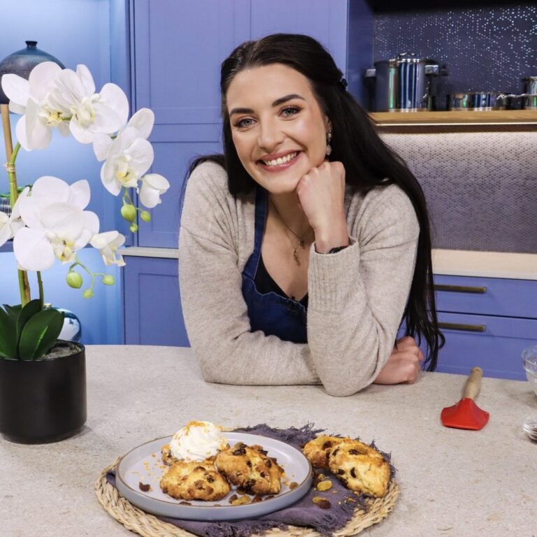 Dani Speek smiling at a kitchen counter with a plate of scones